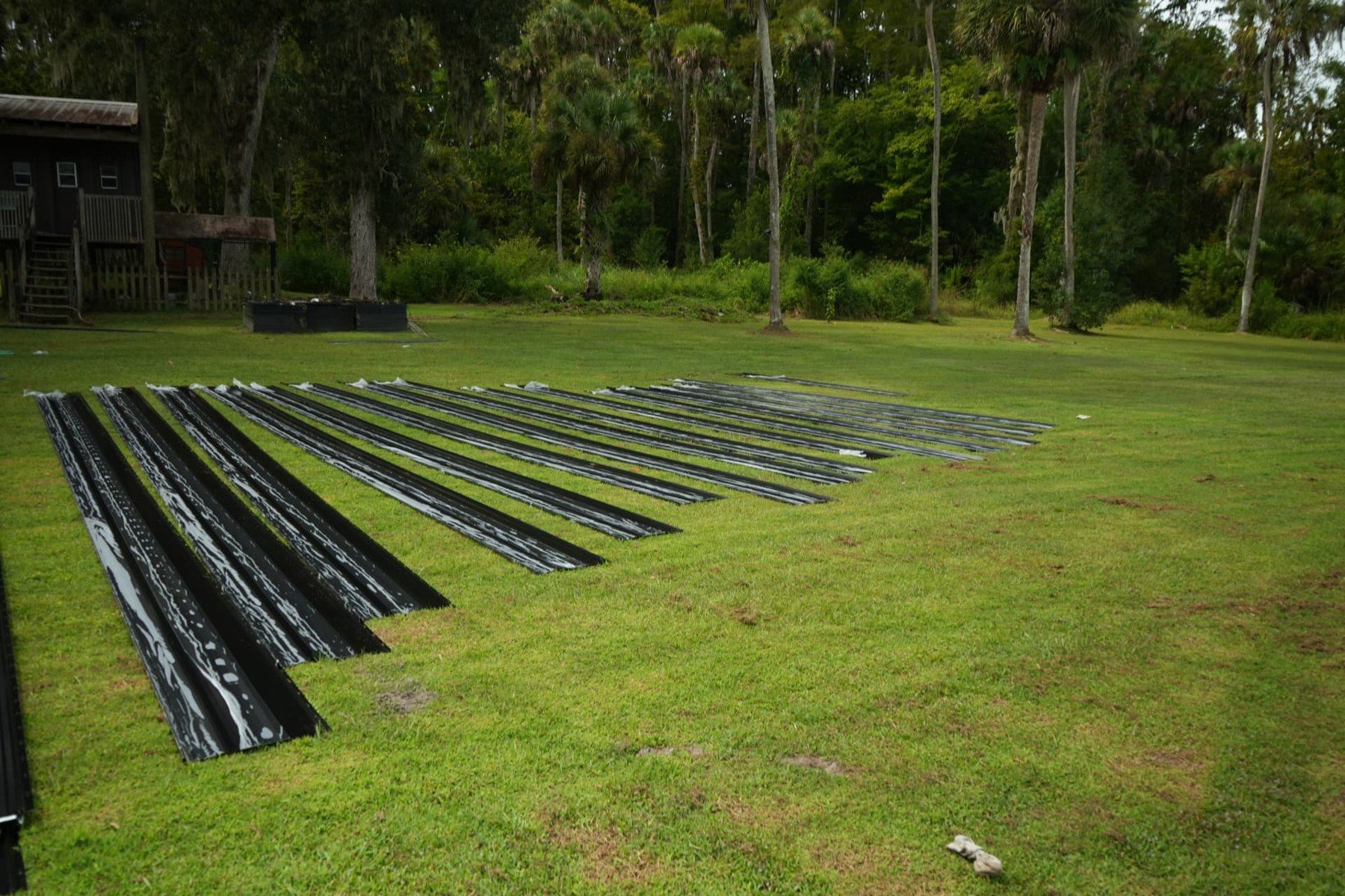 Rows of dark metal roofing panels laid out on grass at the Kissimmee commercial job site